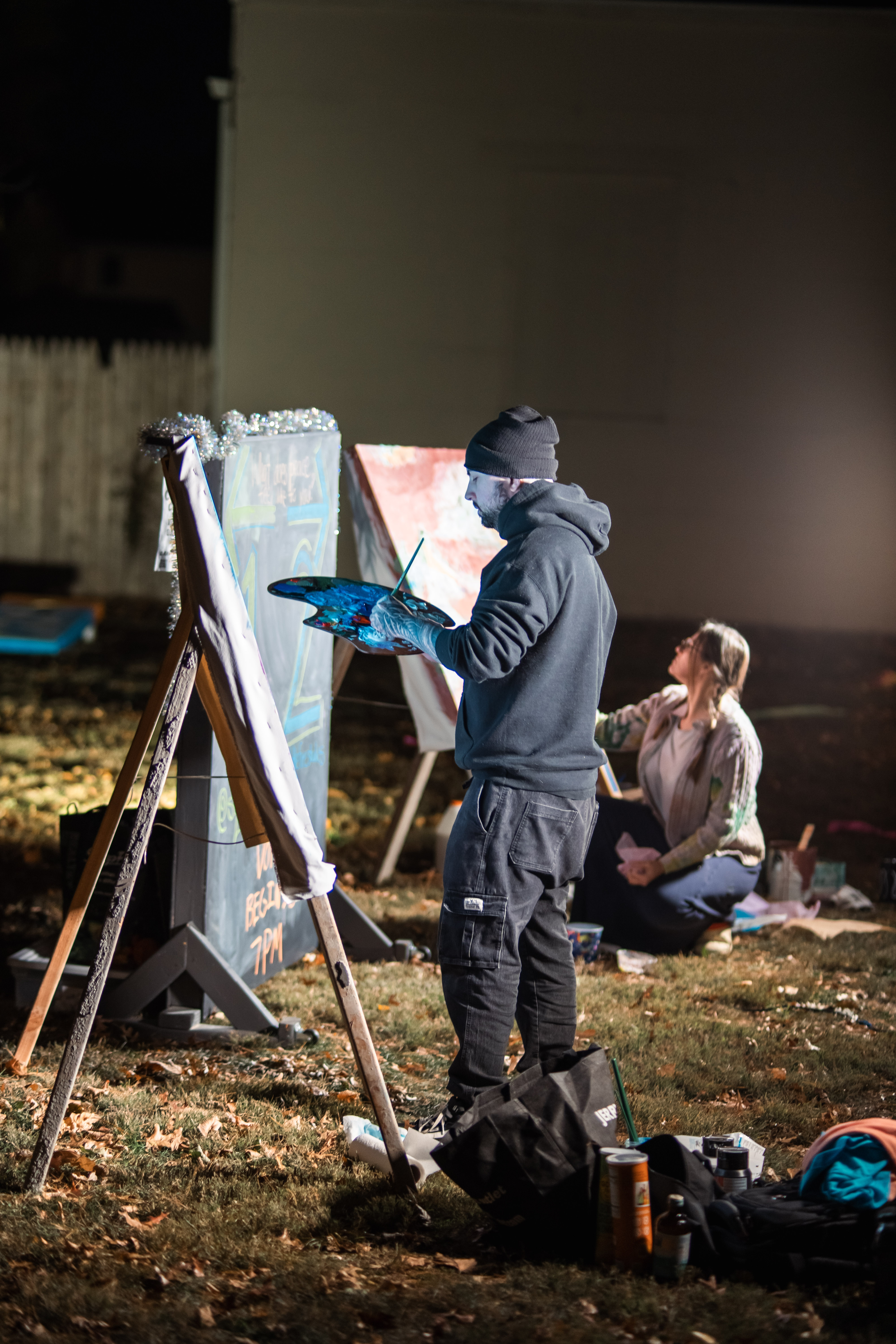 Artist painting outside under lights on a chilly fall evening at DIY